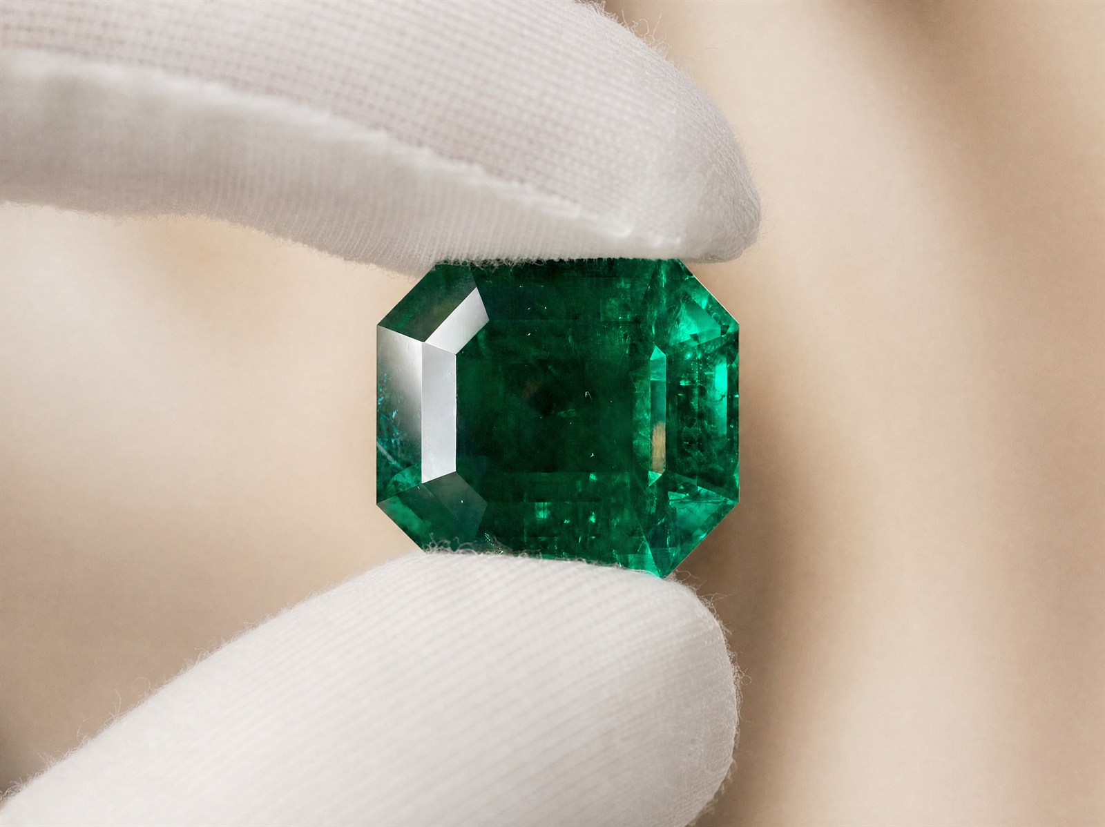 A faceted emerald held between gloved fingertips